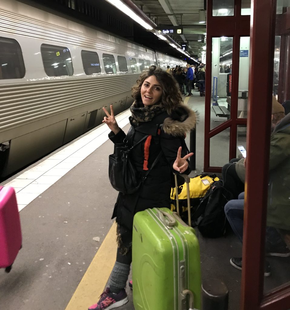 Tren istasyonunda yeşil bir bavul ile beklerken zafer işareti yaparak poz veren kız görüntüsü.