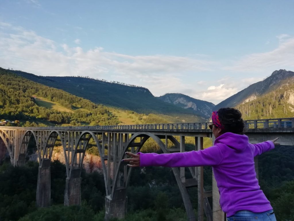 Ellerini iki yana açıp, köprü ve doğaya doğru poz veren bir kadın.
