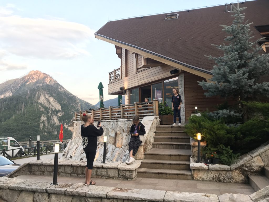 Dağ manzaralı bir otel ve otelin merdivenlerinde fotoğraf çektiren genç kez.