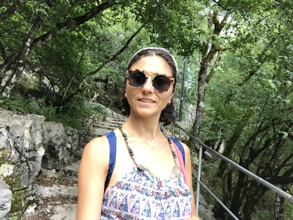 Yeşillikler içinde patika bir yolda merdivenleri çıkarken gülümseyerek poz veren bir kadın.