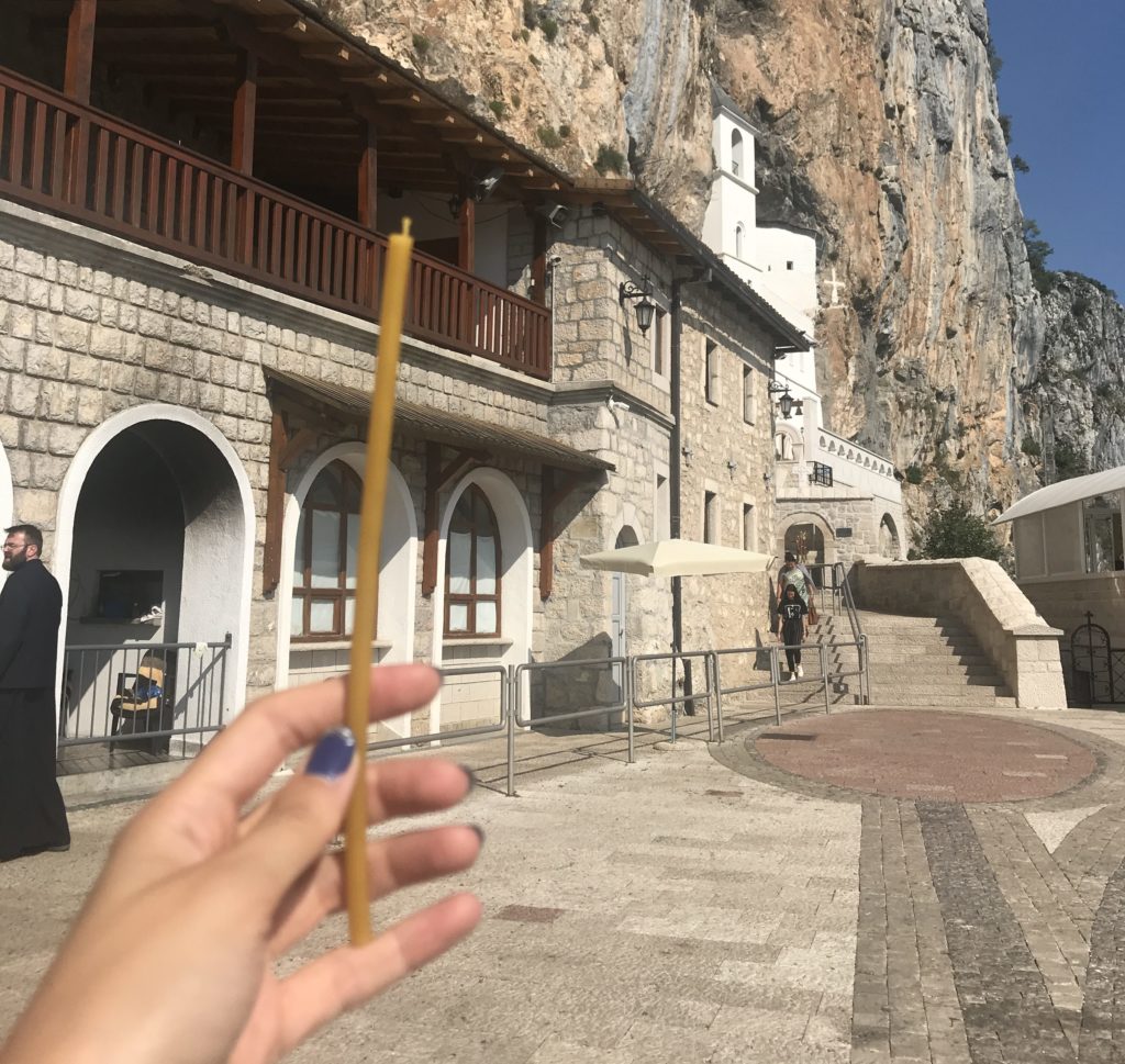 Elinde sarı renkte dilek mumu ile manastırın üst bölümüne doğru çekilmiş bir görüntü.