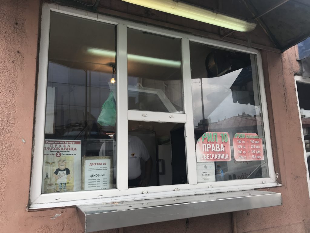 Belgrad'da ne yenir ? yazısından beyaz renkli pimapen bir camın üzerinde çeşitli yazıların yer aldığı, küçük bir restoranın önünde çekilmiş görüntü.