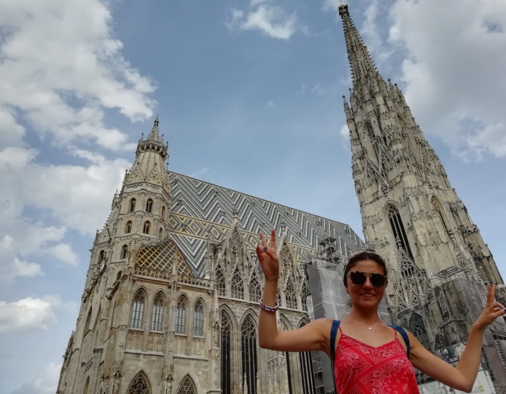 İhtişamlı bir görüntüye sahip katedral önünde eliyle zafer işareti yaparak poz veren bir kadın görüntüsü.