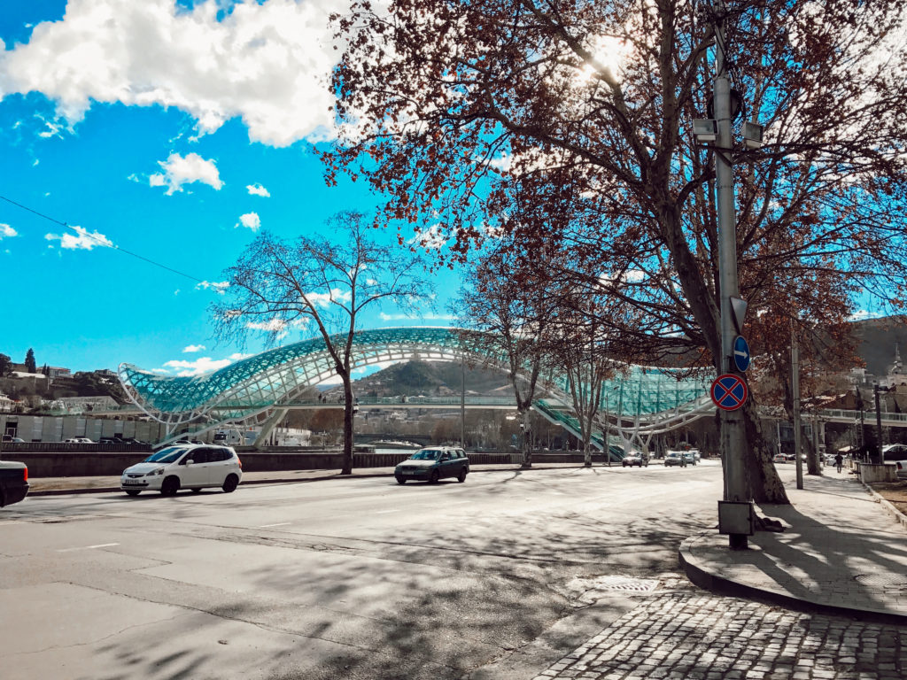 Modern bir, yaprakları sararmış ağaçlar,trafikte seyir halindeki araçların yer aldığı görüntü.