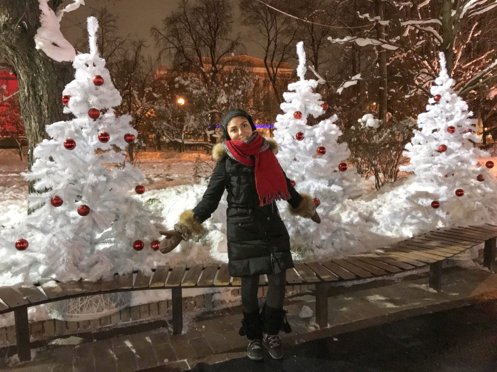 Akam park içerisinde, beyaz çam ağaçları ve kırmızı süsler ile ellerini yana açıp poz veren GezginStar'ın görüntüsü.
