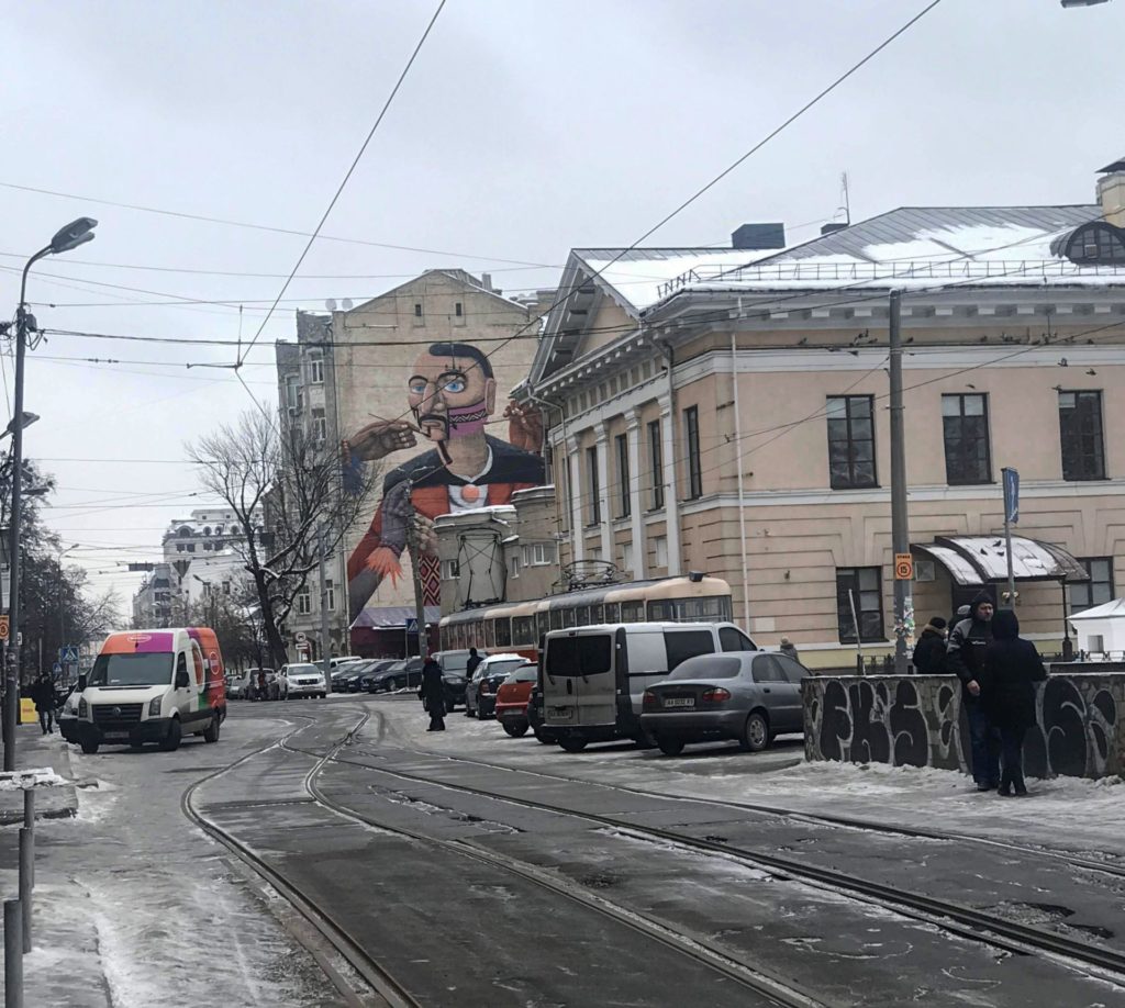 Tramvay yolu, park halindeki araçlar ve binanın yan duvarı üzerinde yer alan Mural görüntüsü.