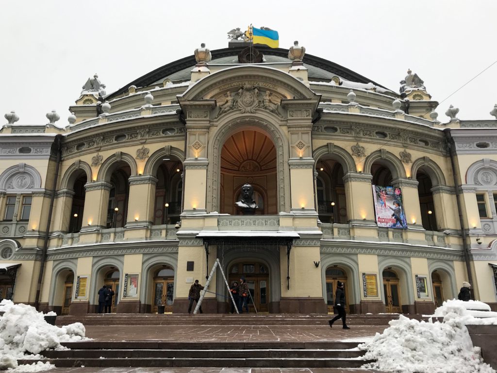 Merdiven yanlarında birikmiş karlar, krem rengi tarihi bir bina ve sarı renkte ışıklandırma ile Kiev'in Ulusak Opera Binası'nın görüntüsü.