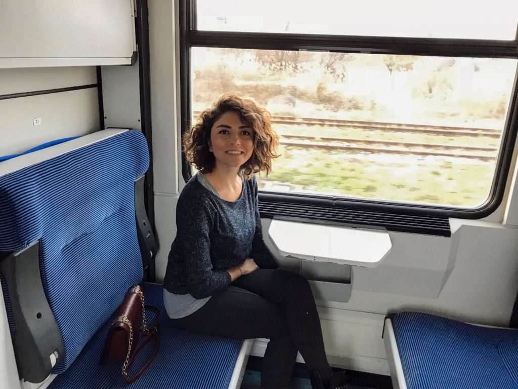 Tren vagonunda, mavi renkteki cam kenarındaki koltukta oturup gülümseyerek poz veren GezgiStar'ın görüntüsü.
