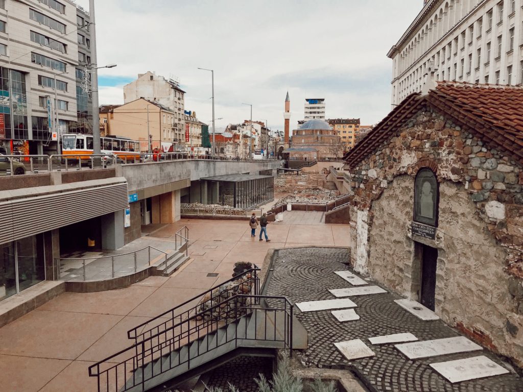 Uzakta minaresi görünen bir cami ve şehir görüntüsünün yer aldığı fotoğraf.