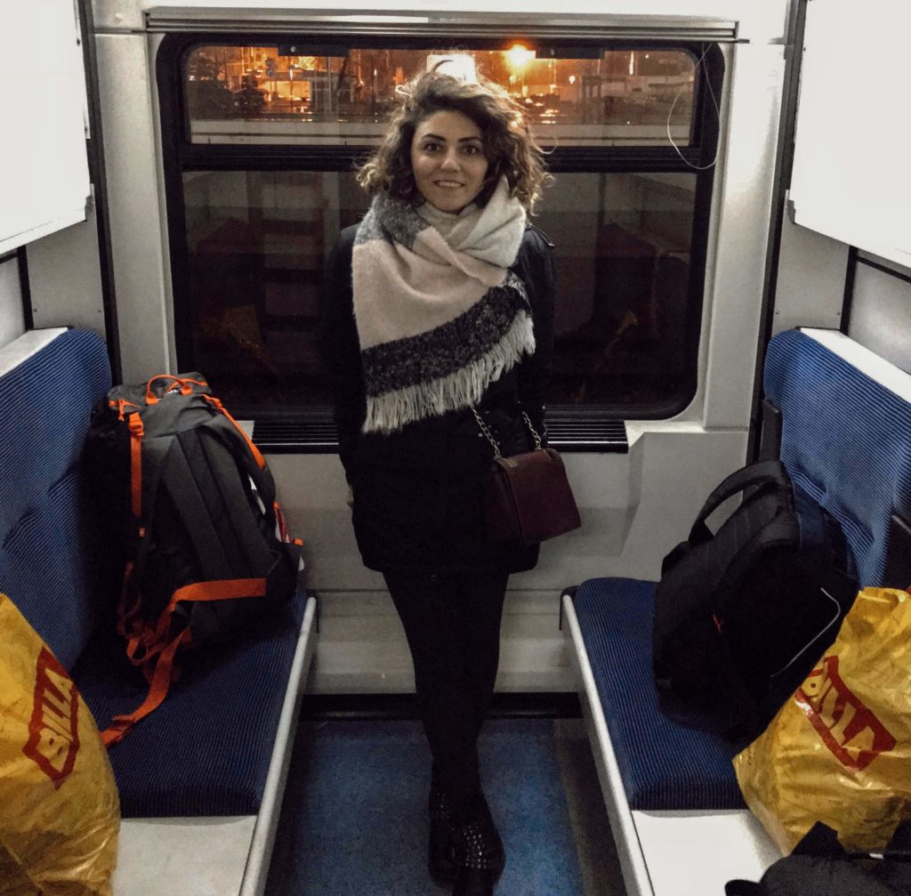 Tren vagonunda koltuklara konulmuş sırt çantası ve poşetler ile ayakta durup poz veren bir kadın görüntüsü.