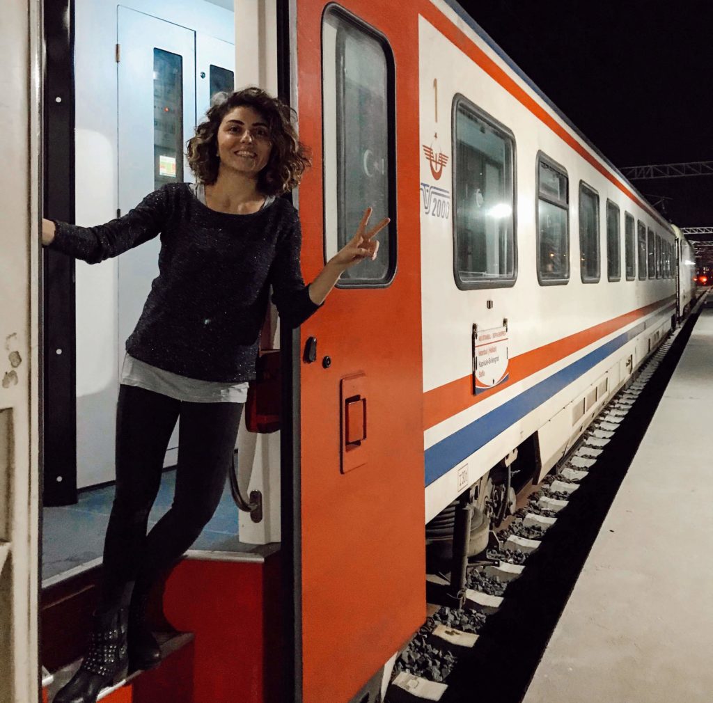 Tren vagonunda kapıya omzunu yaslayıp gülümseyerek poz veren bir kadın görüntüsü.