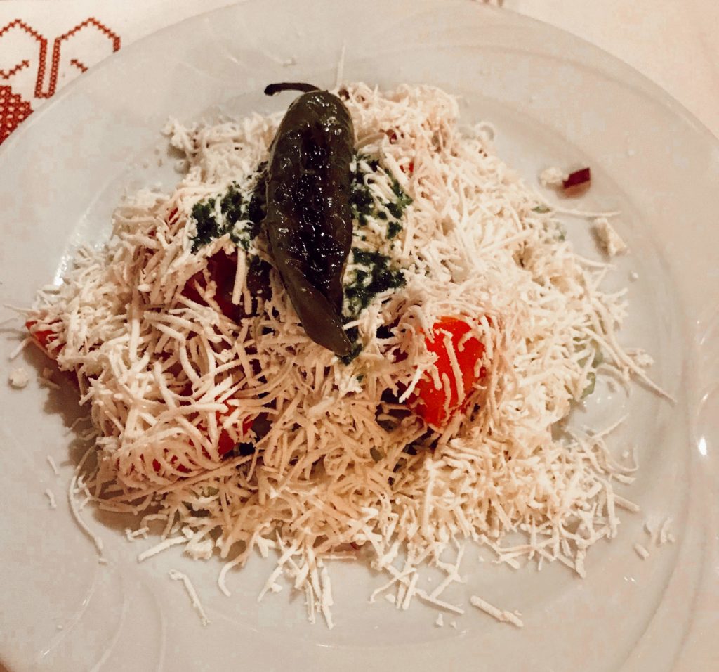 Beyaz bir tabak içerisine hazırlanmış salata ve üzerinde kızarmış yeşil biber ve peynirin yer aldığı görüntü.
