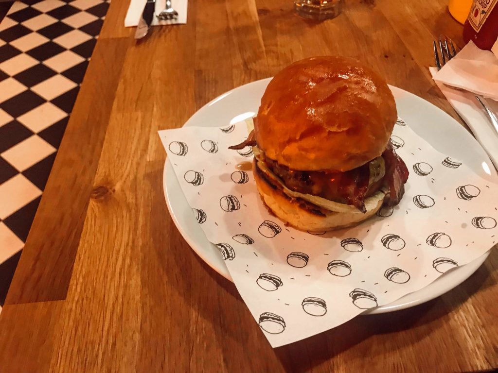 Tabak içerisinde servis edilen, oldukça büyük olarak hazırlanmış bir hamburger görüntüsü.