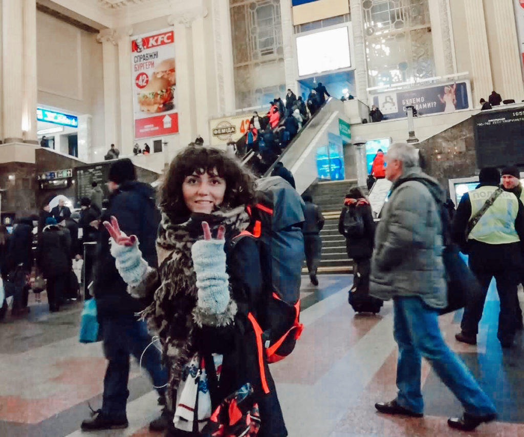 Tren garında, kalabalıkta sırt çantası ile gülümseyip poz veren kadının Kiev'e ulaşım yazısından görüntüsü.