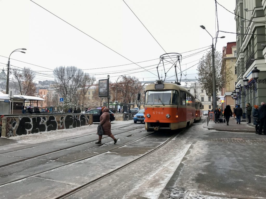 Kırmızı renkte bir tramvay ve karşıdan karşıya geçen bir kadının yer aldığı Kiev şehrinden bir görüntü.