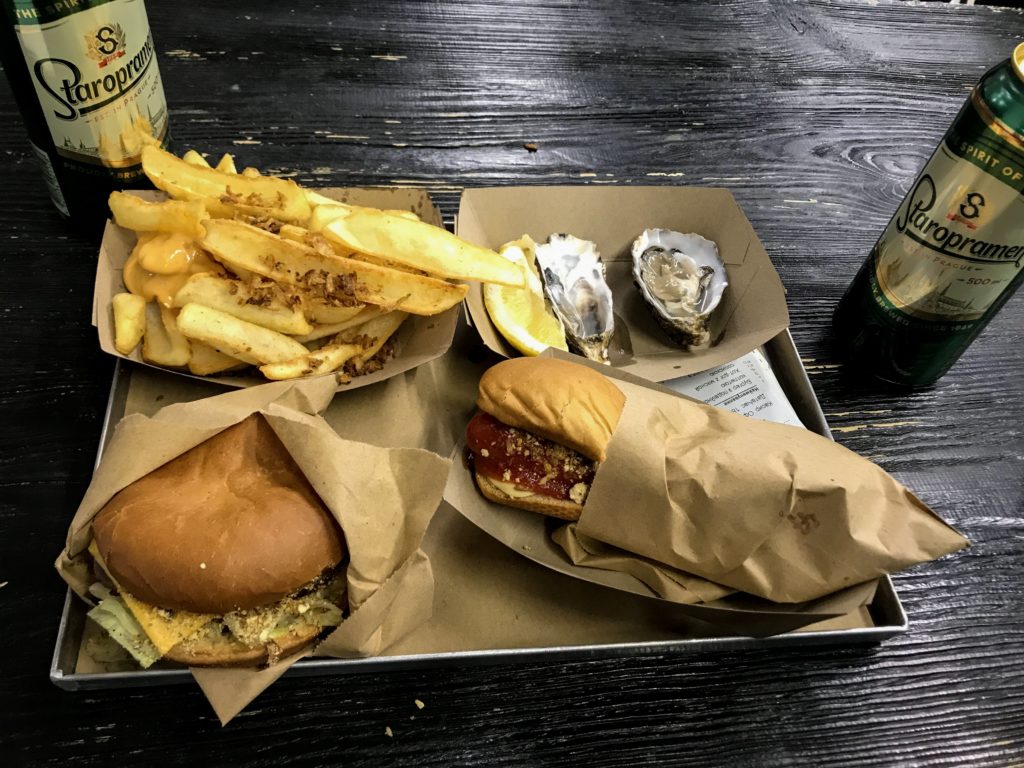 Tepsi içerisinde hamburger, hotdog, patates kızartması ve istiridyenin yer aldığı yiyeceklerin görüntü.