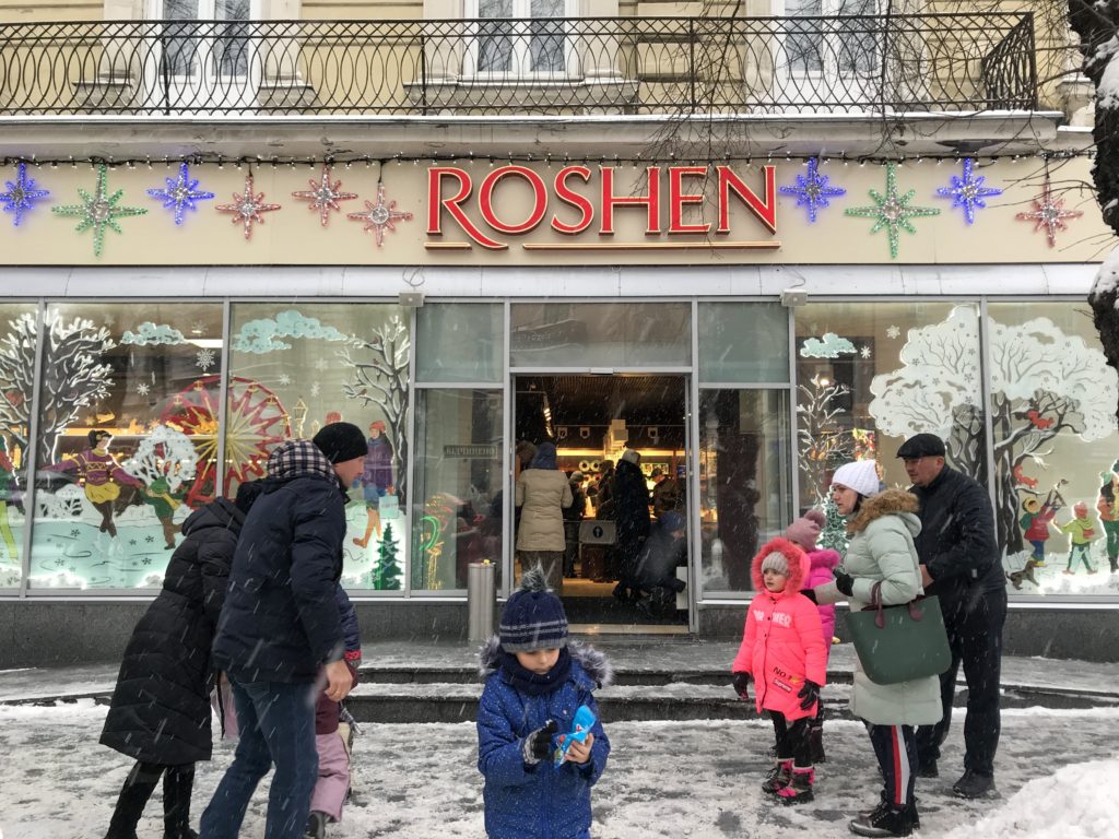 Roshen mağazası önünde, yağan kar altında mağazaya giren insanların görüntüsü.