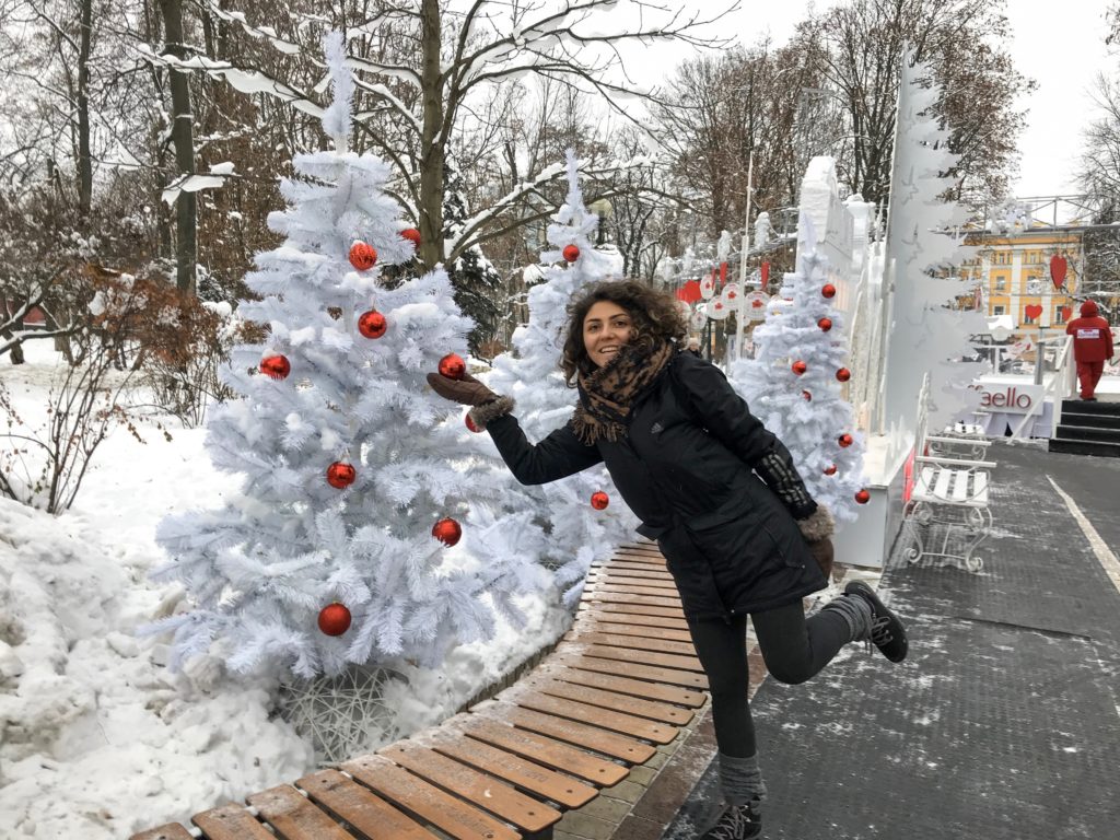 Beyaz çam ağaçları ve üzerindeki kırmızı süsleri tutup gülümseyerek poz veren bir kadının görüntüsü. 