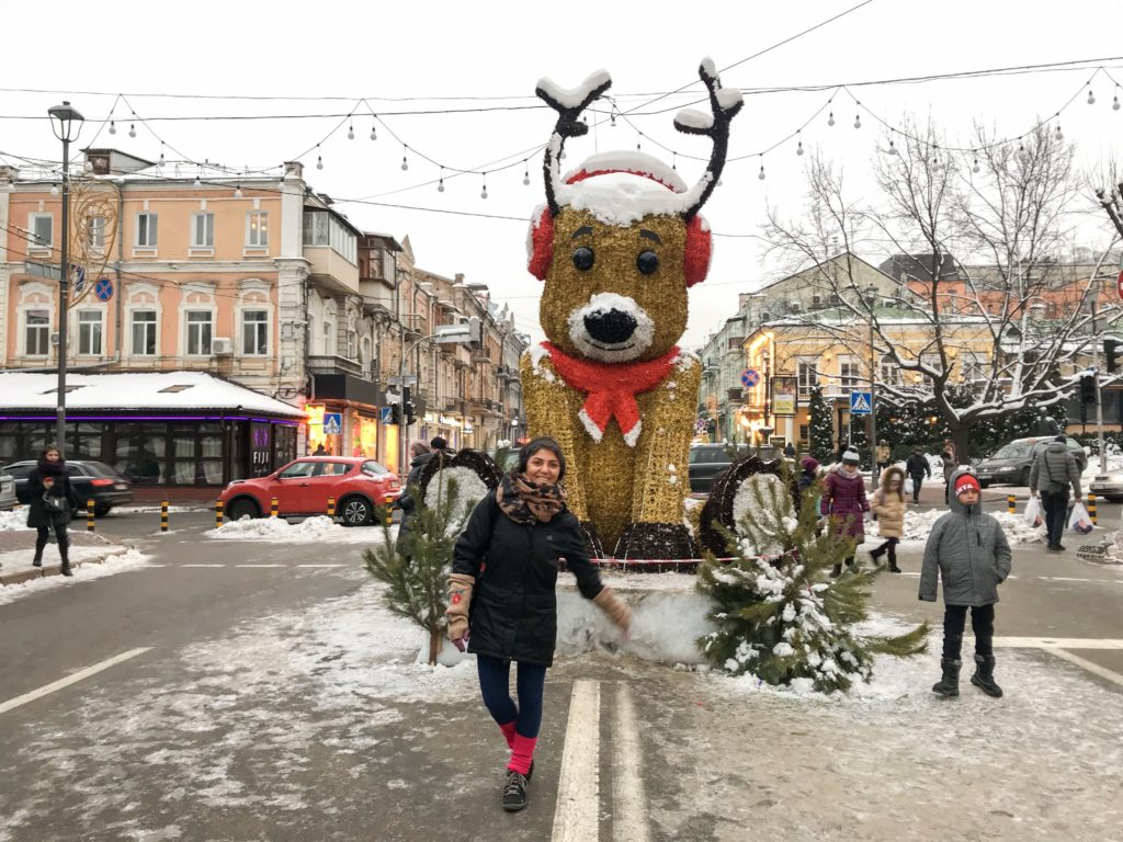 Karla kaplı bir yolda, arkasından özel tasarlanmış kocaman bir yen yıl konseptinde giydirilmiş köpek objesiönünde poz veren kadın.