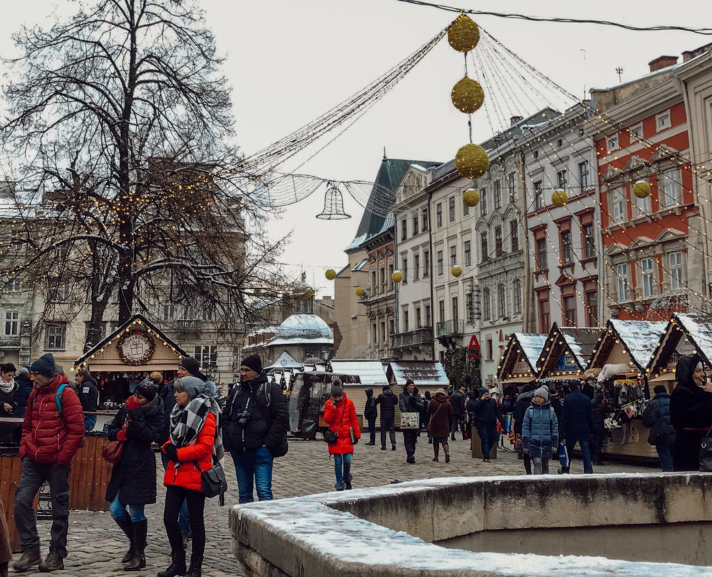 Trafiğe kapalı bir yolda, yılbaşı için süslenmiş sokakta noel pazarı gezen insanların yer aldığı görüntü.