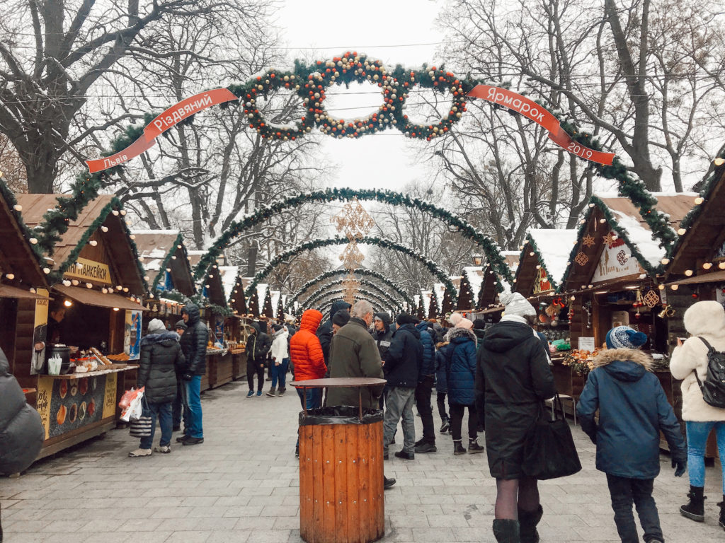Karşılıklı ahşap kulübeler arasında yürüyen insanlar, yılbaşı için süslenmiş tezgahların yer aldığı noel pazarı görüntüsü.