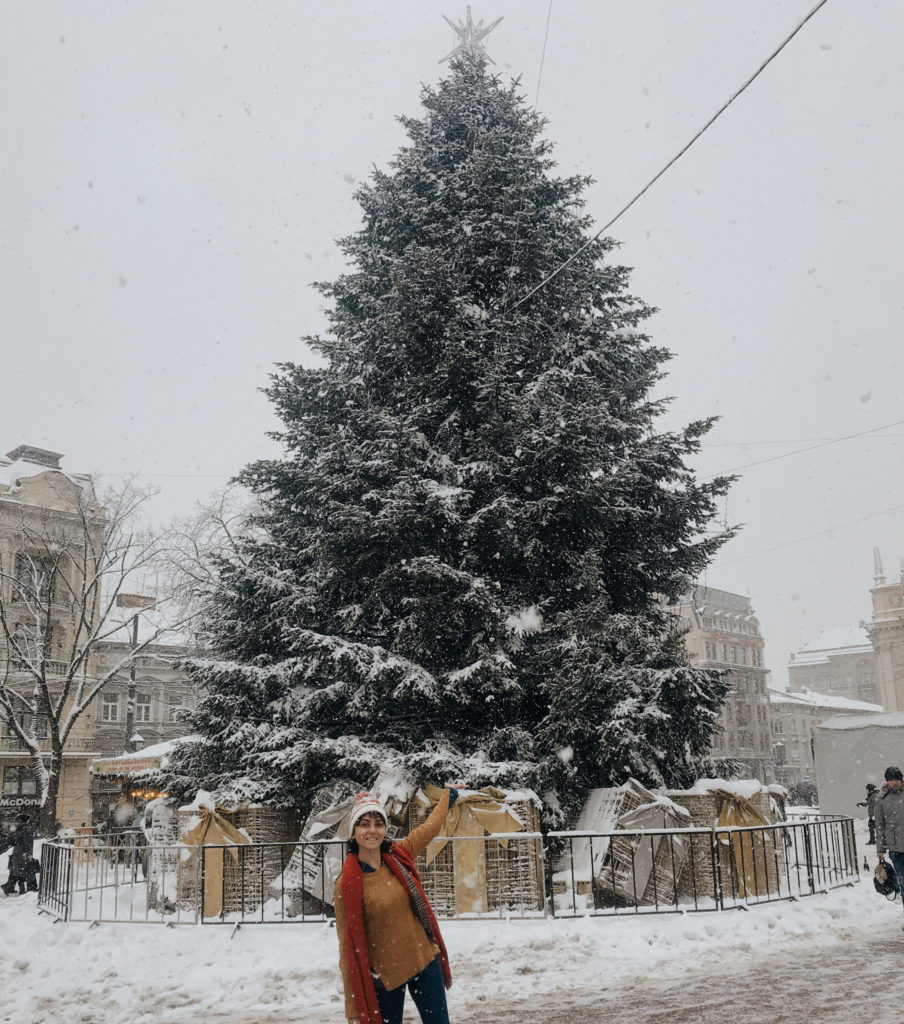 Şehir meydanına yerleşitrilmiş kocaman noel ağacı önünde poz veren kadın.