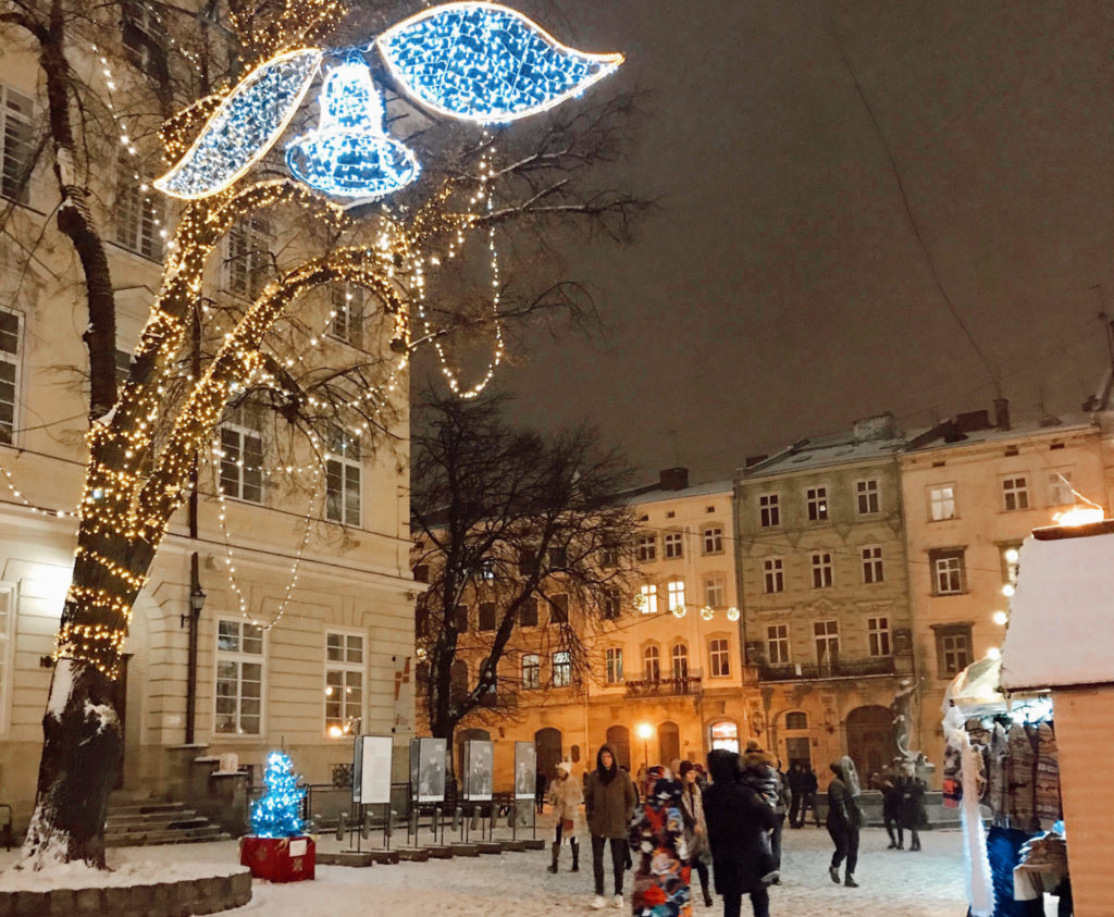 Ağaçların yılbaşı için ışıklandırıldığı, ahşağ kulübelerin yer aldığı noel pazarını gezeninsanlarında yer aldığı Lviv şehrindenbir görüntü.