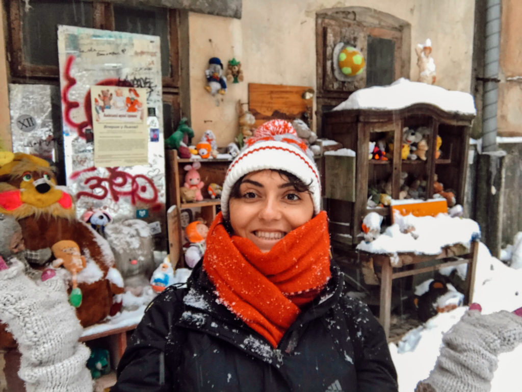 Birbirinden farklı oyuncakların önünde ellerini iki yana açıp, gülümseyerek poz veren bir kadın görüntüsü.