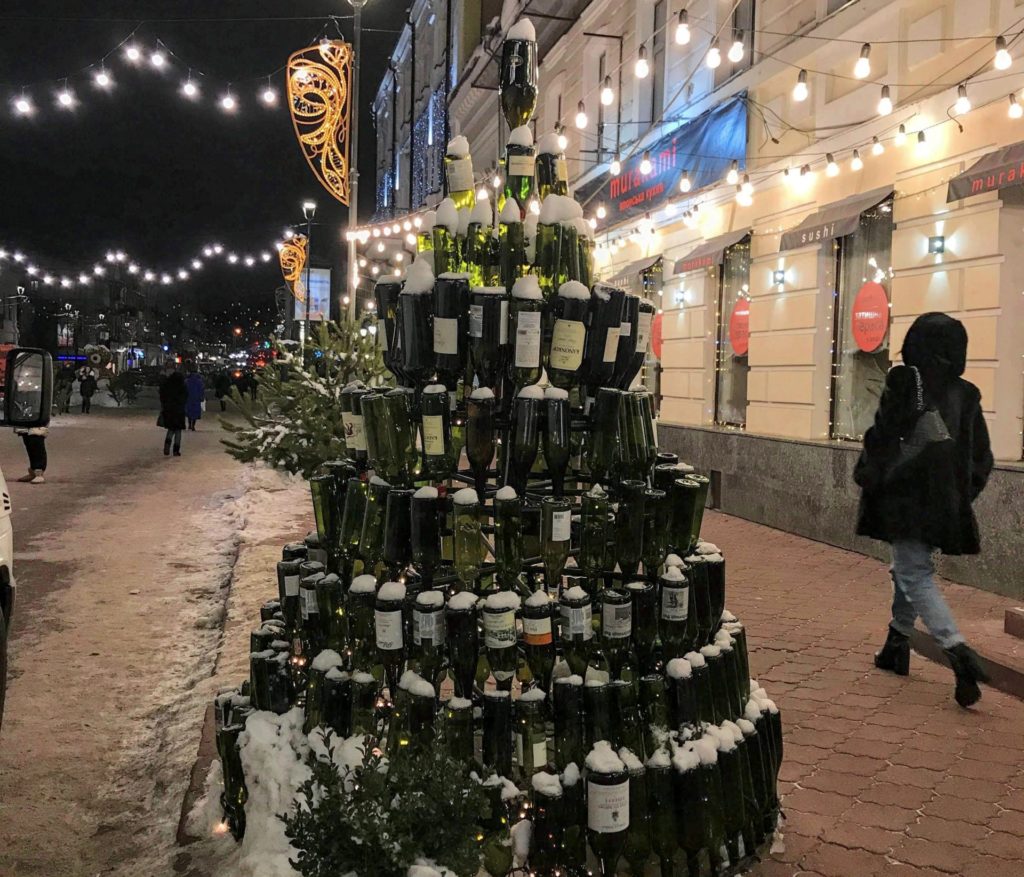 İçki şişlerinden tasarlanmış bir noel ağacı ve ışıklarla aydınlatılmuış bir sokaktan görüntü.
