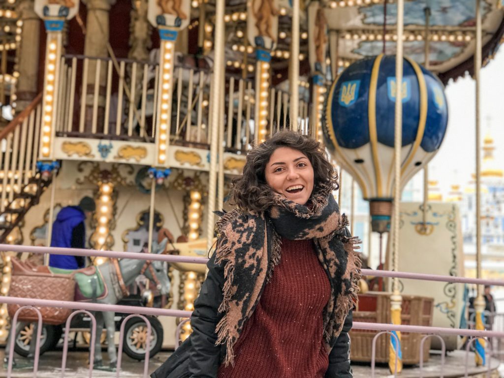 Işıklarıyla etrafı aydınlatan, sarı,mavi,kırmızı renklerdeki atlı karınca önünde gülümseyerek poz veren bir kadın.