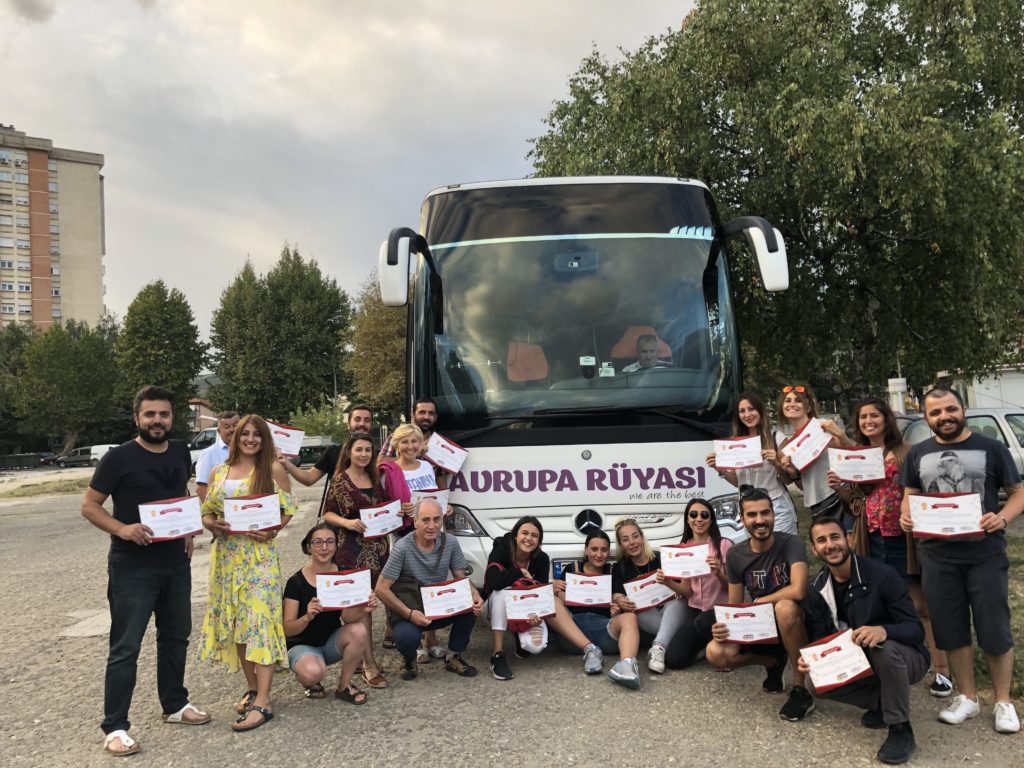 Seyahat otobüsü önünde, yolcuların ellerinde kağıt tutup verdikleri bir poz.